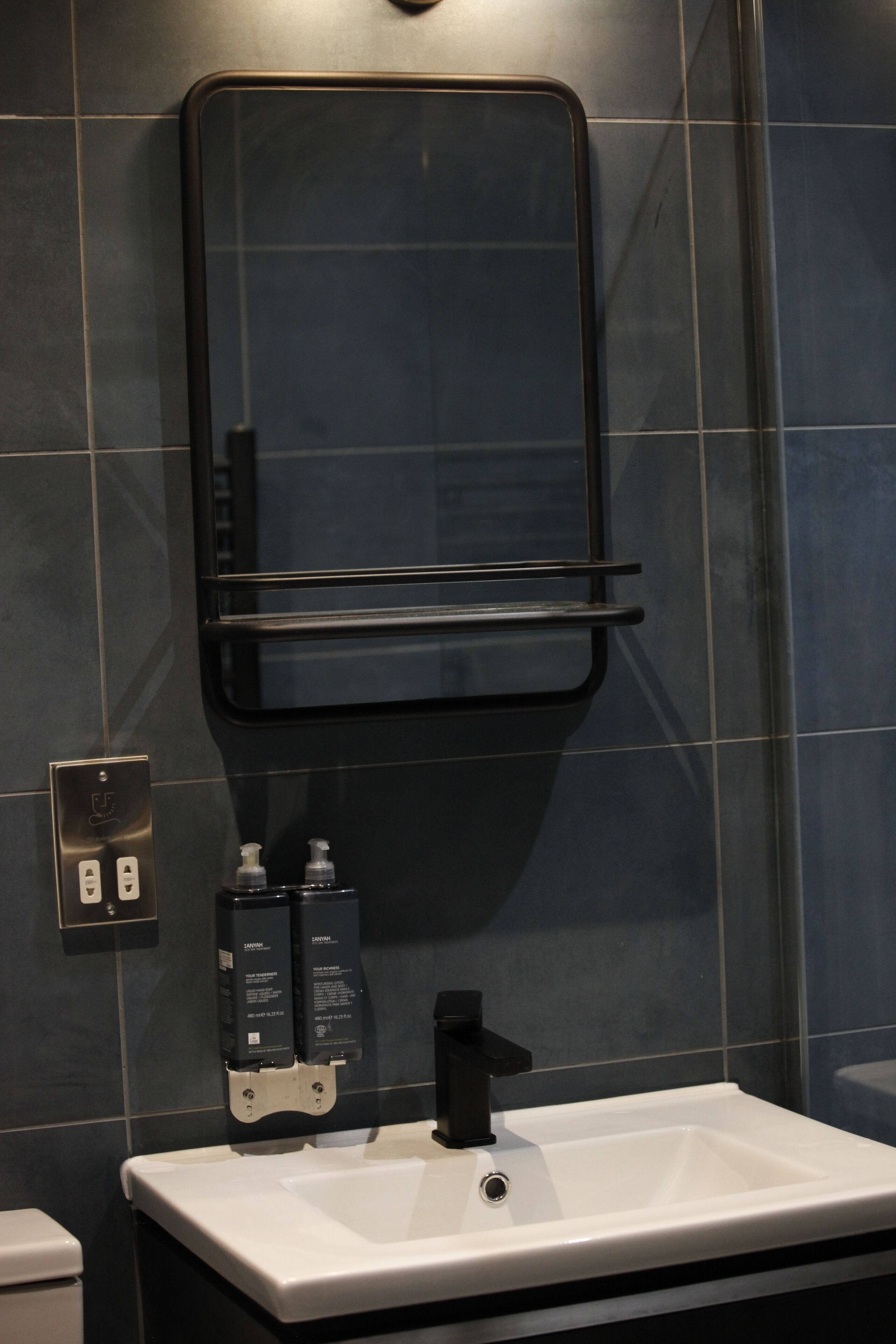 A bathroom with a white sink, black faucet, and a mirror above it. There are two soap dispensers on the wall.
