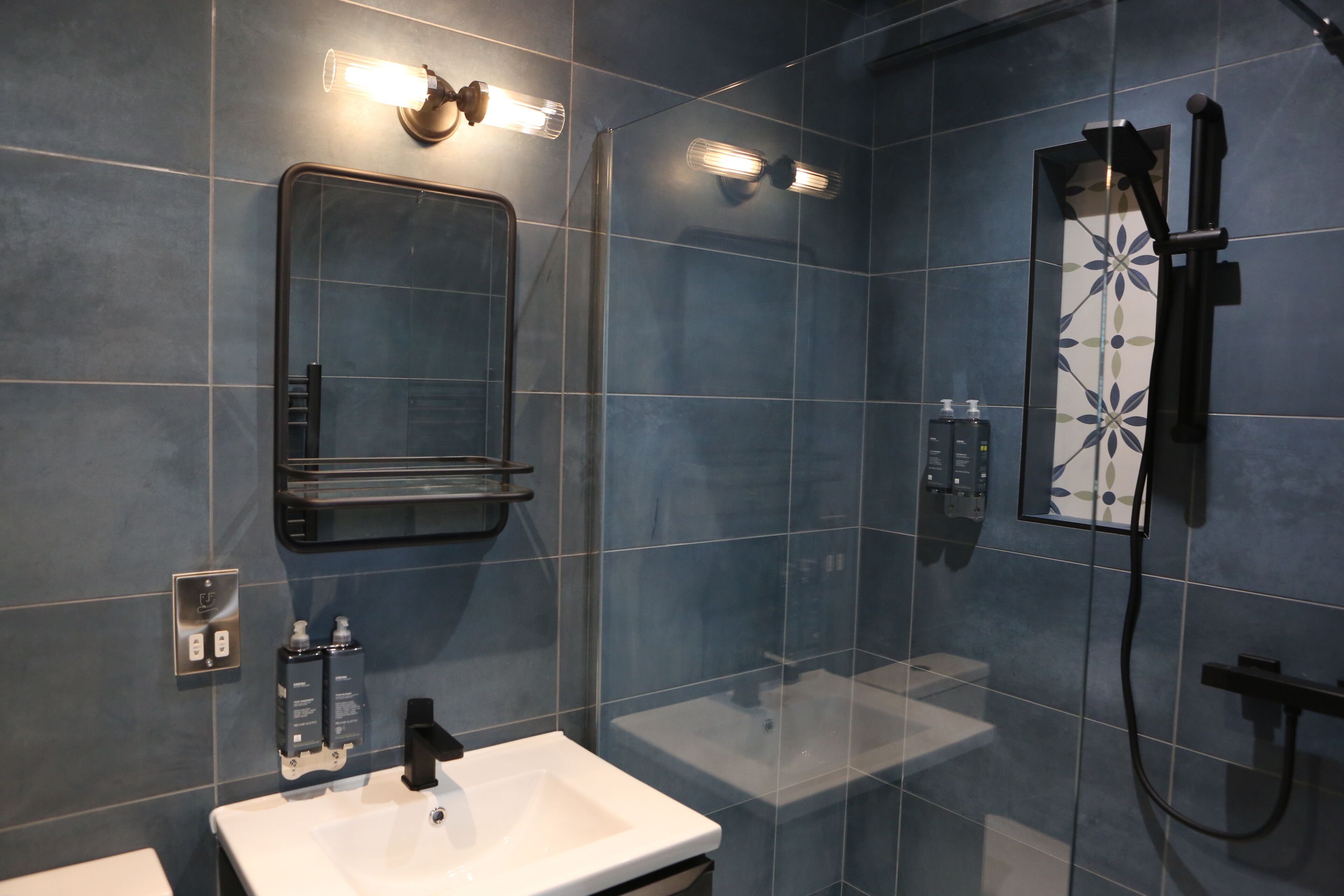 Une salle de bain moderne avec un lavabo blanc, une cabine de douche en verre et un miroir doté d’un éclairage intégré.