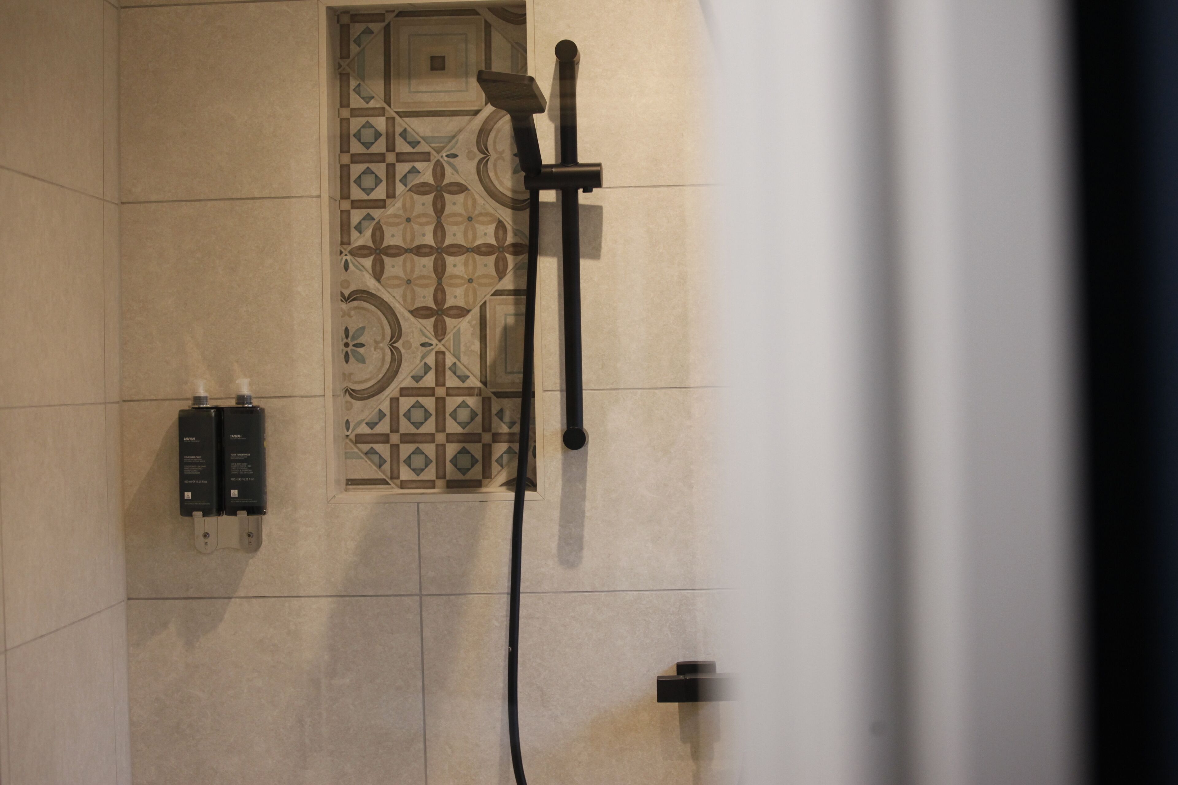 A shower area with a patterned tile wall, a handheld showerhead, and a wall-mounted control panel.