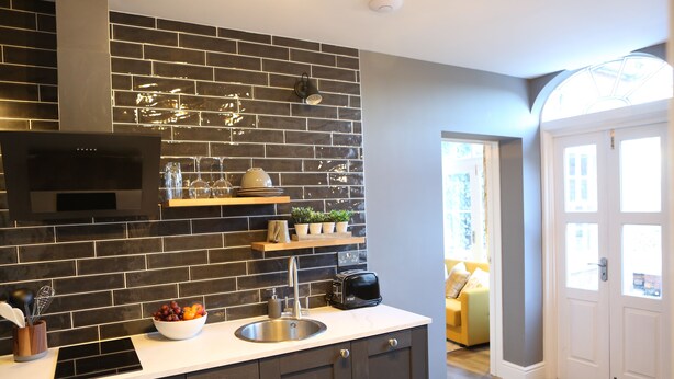 Una cocina moderna con salpicadero de azulejos oscuros, electrodomésticos de acero inoxidable y encimera blanca.