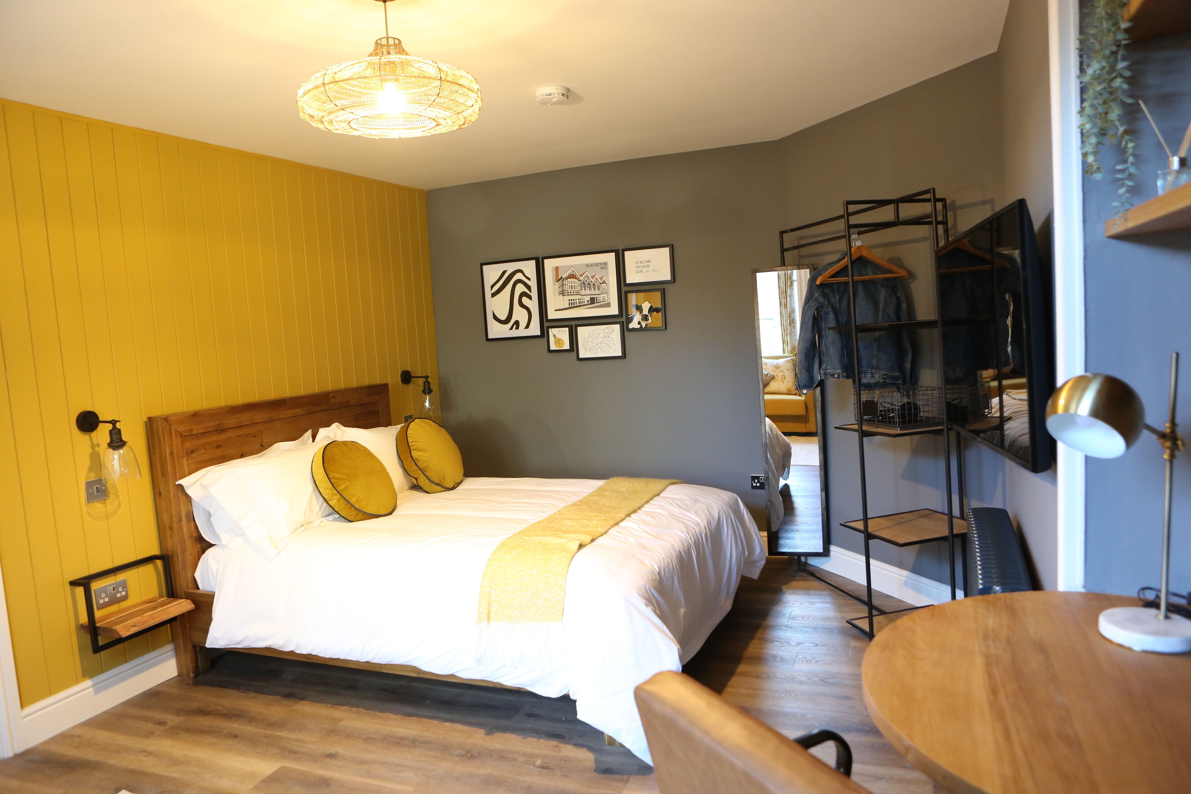 A neatly arranged bedroom with a bed, bedside tables, a hanging clothes rack, and wall-mounted artwork.
