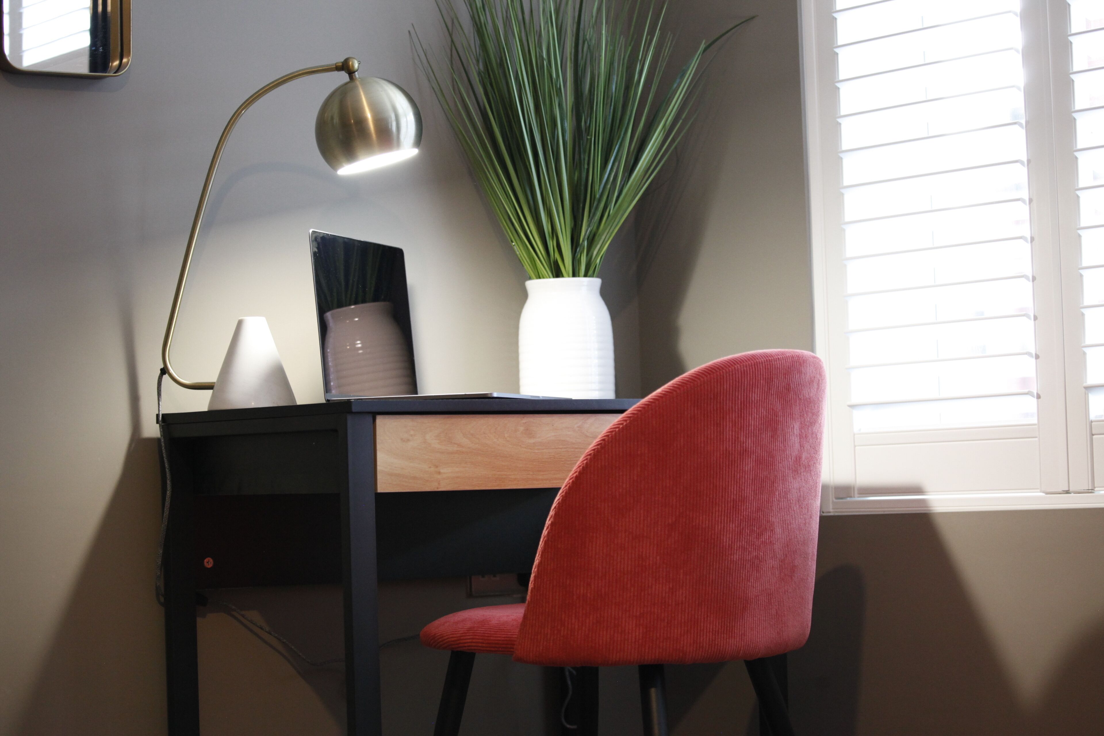 Ein Schreibtisch mit einer Lampe, einem Topfpflanzen und einem roten Stuhl.