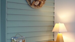 Un meuble en bois surmonté d’une lampe, un chapeau accroché au mur et un petit objet décoratif posé sur le meuble.