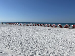 Une plage bordée de rangées de parasols rouges et blancs et de chaises de plage.