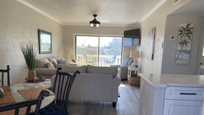 A modern living room with a sofa, dining table, chairs, and a kitchen area. - Remodeled Beach Oasis (Ormond Beach)