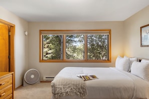 A bedroom with a large window, a bed with white bedding, a fan, and a wooden door.