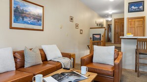 Un salon avec un canapé en cuir marron, une table basse sur laquelle repose un magazine et un tableau représentant un paysage de montagne.
