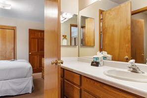 Une chambre d’hôtel avec un lit double, une armoire en bois, une salle de bain avec un lavabo et un miroir, et des articles de toilette posés sur le comptoir.