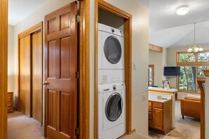 Une buanderie équipée d’un lave-linge et d’un sèche-linge superposés, de portes en bois et d’un coin cuisine avec une fenêtre.