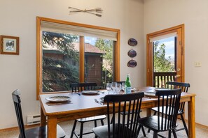 A dining area with a wooden table, black chairs, and a view of a house through large windows.