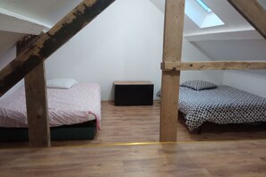 Cozy attic-style bedroom with two single beds, a bedside table, and storage unit, set amidst rustic wooden beams and flooring.