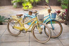 Deux vélos sont garés sur une terrasse, avec une clôture en bois et des plantes en arrière-plan.