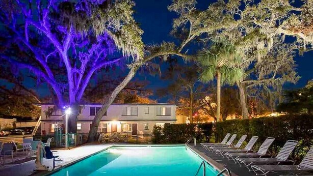 Piscina com cadeiras de descanso e um edifício ao fundo.