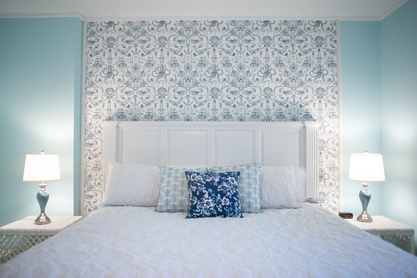 A bedroom with a white bed, blue floral wallpaper, and two bedside tables with lamps.