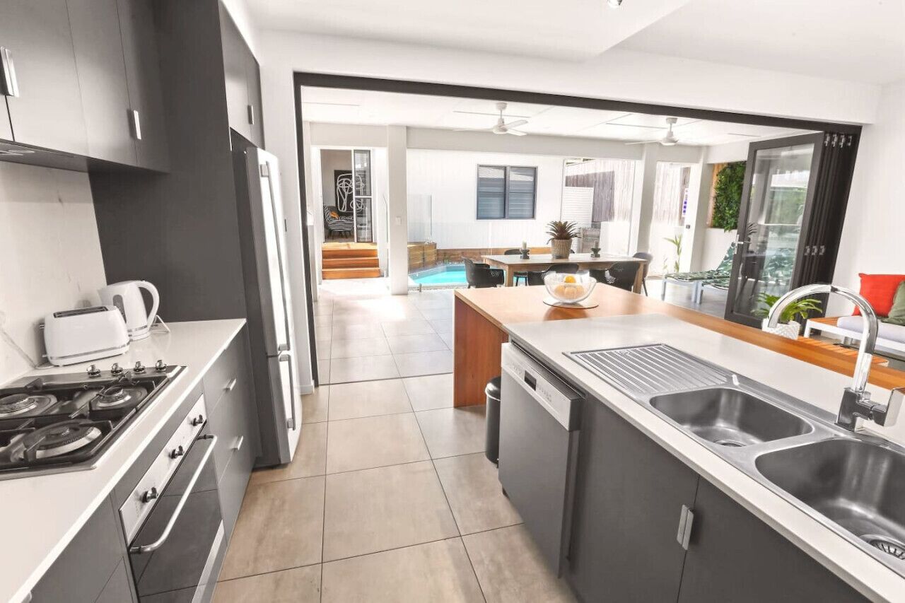 A modern kitchen with a central island, a dining area with a pool view, and a staircase leading to a balcony.