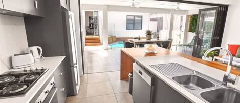 A modern kitchen with a central island, a dining area with a pool view, and a staircase leading to a balcony.