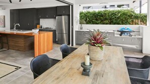 Una cocina moderna con armarios oscuros, un refrigerador de acero inoxidable y un comedor con mesa y sillas de madera.