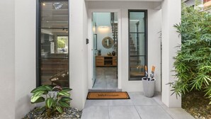 Entrada de una casa moderna con puerta de vidrio, felpudo y planta en maceta.