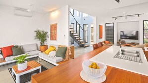 Un salón moderno con sofá, una mesa de centro y una zona de comedor con una isla blanca y una cesta de fruta.