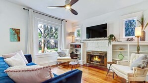 A living room with a fireplace, a ceiling fan, and a TV mounted on the wall. - Uptown Charmer|1mile walk to DT|2miles Vilano BCH (Saint Augustine)