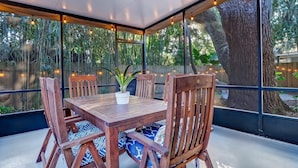 A covered patio with a wooden table and chairs, large windows, and a ceiling fan. - Uptown Charmer|1mile walk to DT|2miles Vilano BCH (Saint Augustine)