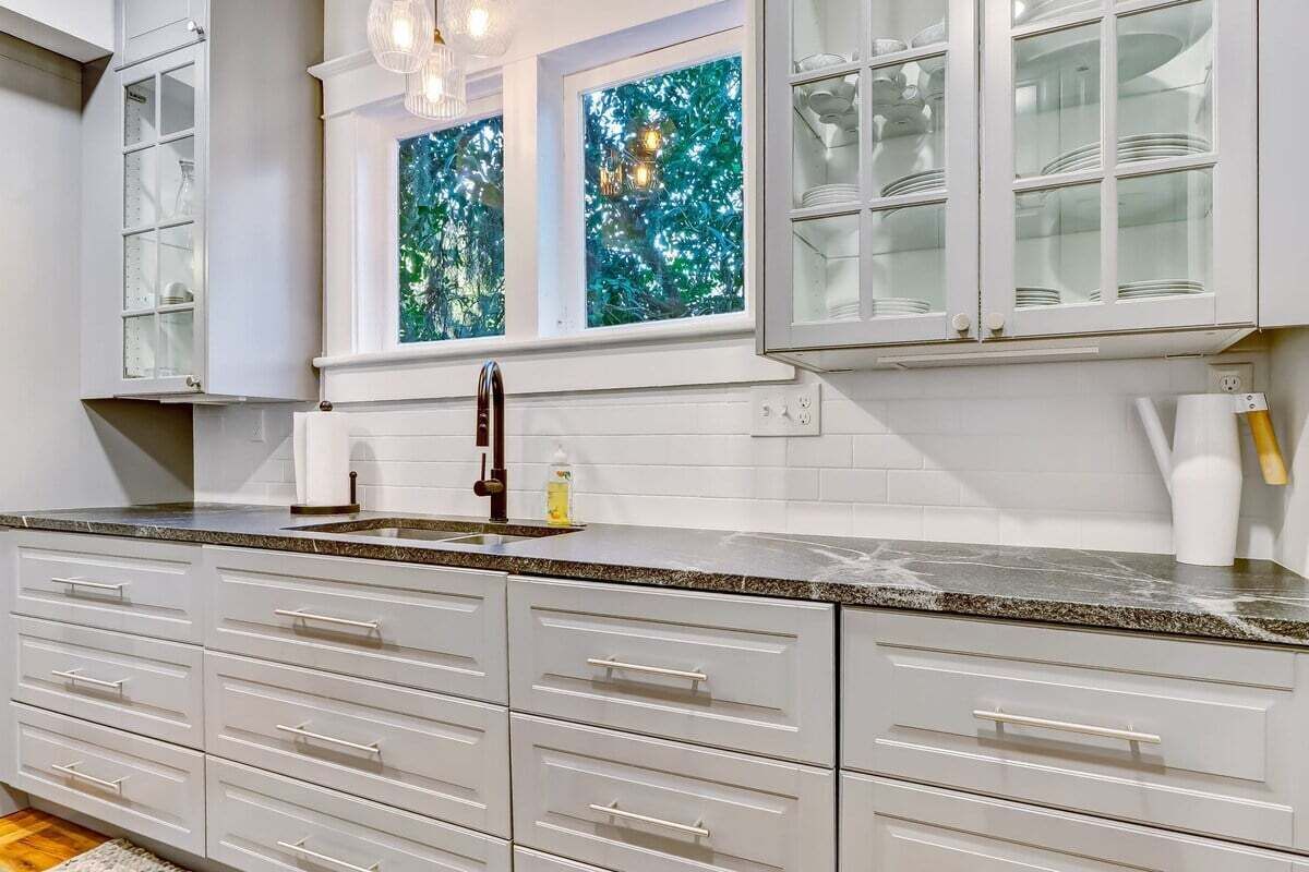 A kitchen with white cabinets, a granite countertop, and a window with a green leafy view.