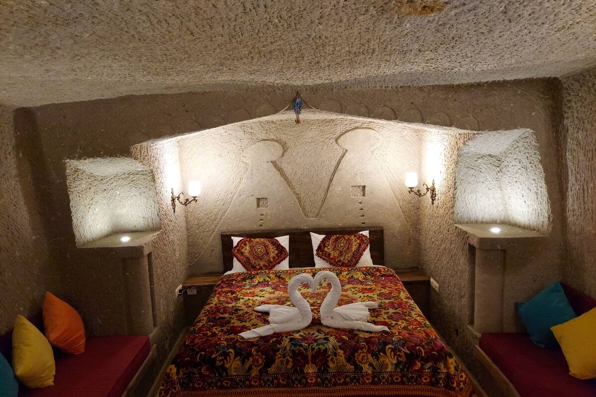 A room with a stone ceiling, a bed with a colorful bedspread, and two wall-mounted lamps.