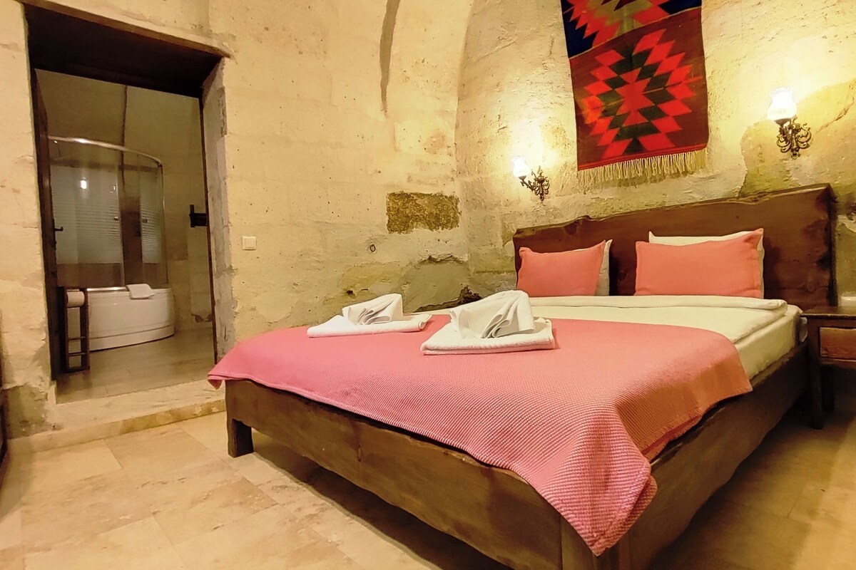 A bedroom with a wooden bed, pink bedding, and a red patterned tapestry on the wall.