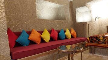 A room with a red sofa, colorful cushions, a glass table, and a patterned bedspread.