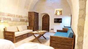 A cozy room with a wooden sofa, a wooden table, and a television mounted on the wall. - Armesos Cave Hotel (Ürgüp)