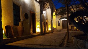 A narrow cobblestone pathway leading to a building with multiple doors and windows, illuminated by warm lighting. - Armesos Cave Hotel (Ürgüp)