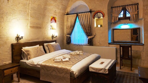 A traditional room with a bed, bedside table, and a small stool. - Armesos Cave Hotel (Ürgüp)