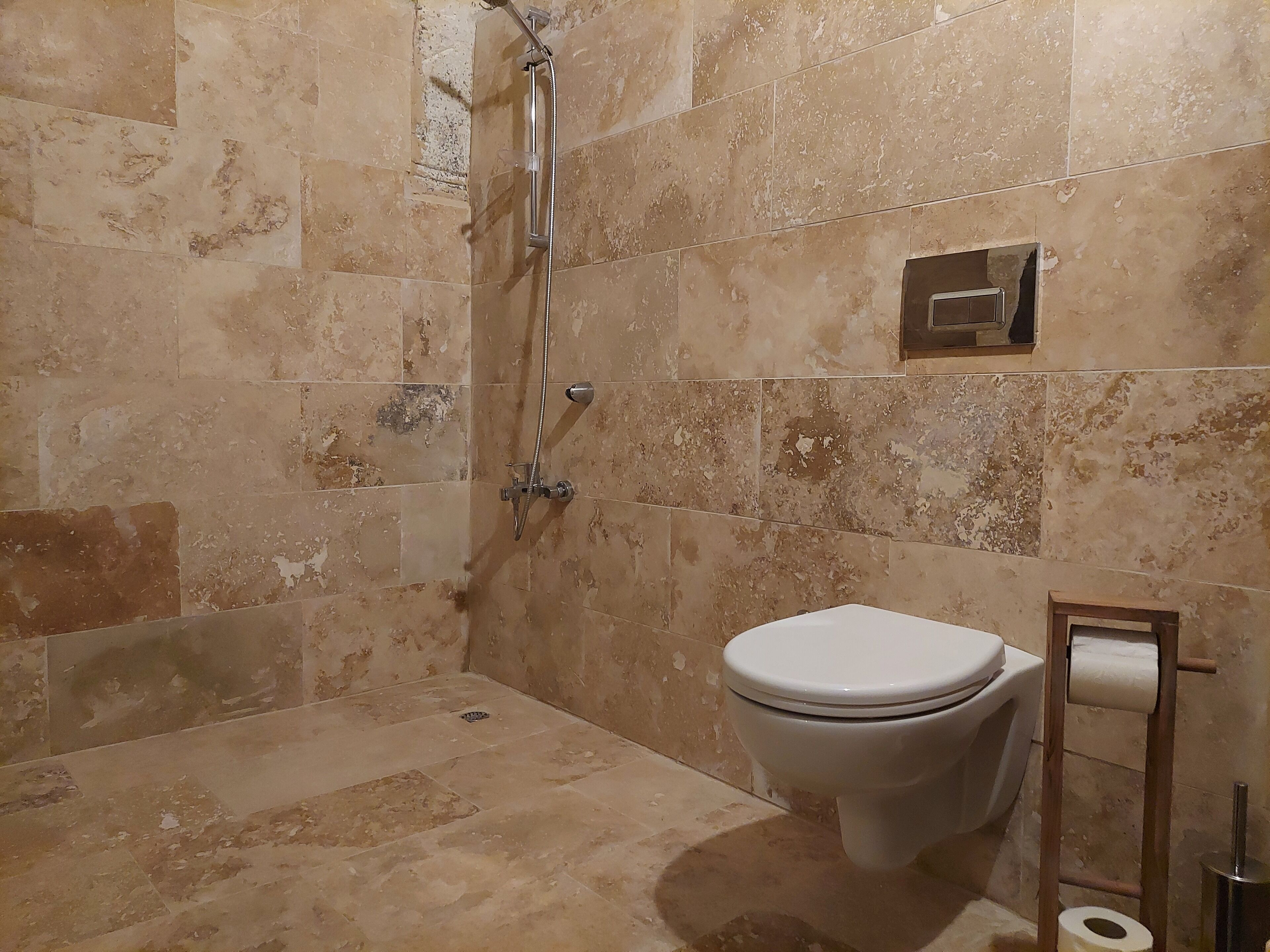 A bathroom with beige tiles, a shower, a toilet, and a toilet paper holder.