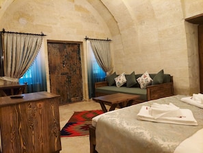 Um quarto acolhedor com porta de madeira, um sofá verde com almofadas florais, uma mesa de madeira e uma cama com toalhas dobradas.