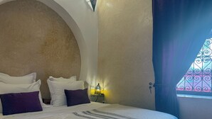 A bedroom with a large bed, a nightstand, a lamp, and a window with decorative iron bars.