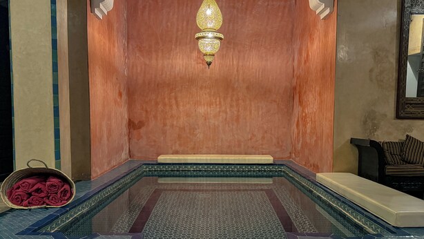 A traditional hammam with a tiled floor, a bench, and a hanging lamp.