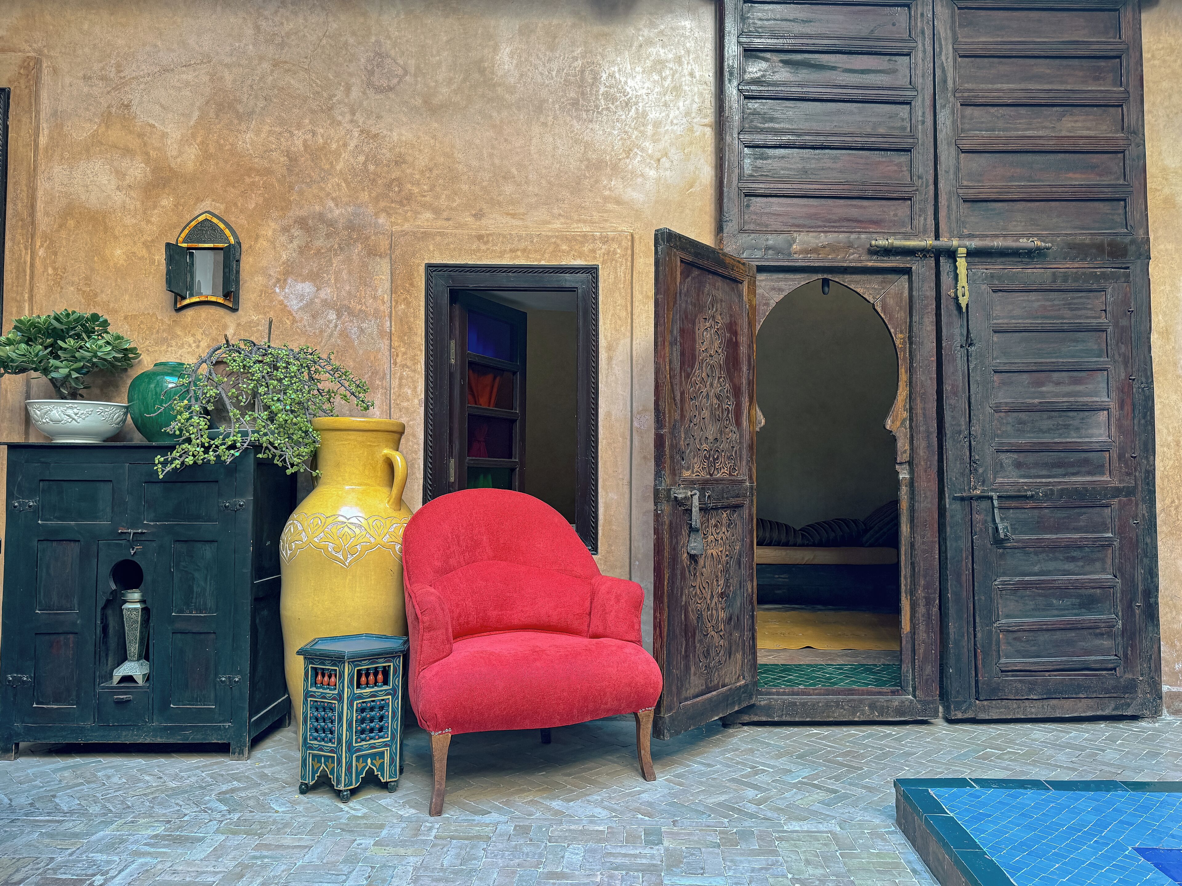 A traditional interior with a red chair, a large yellow vase, and a dark wooden door.