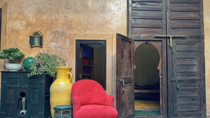 A traditional interior with a red chair, a large yellow vase, and a dark wooden door.