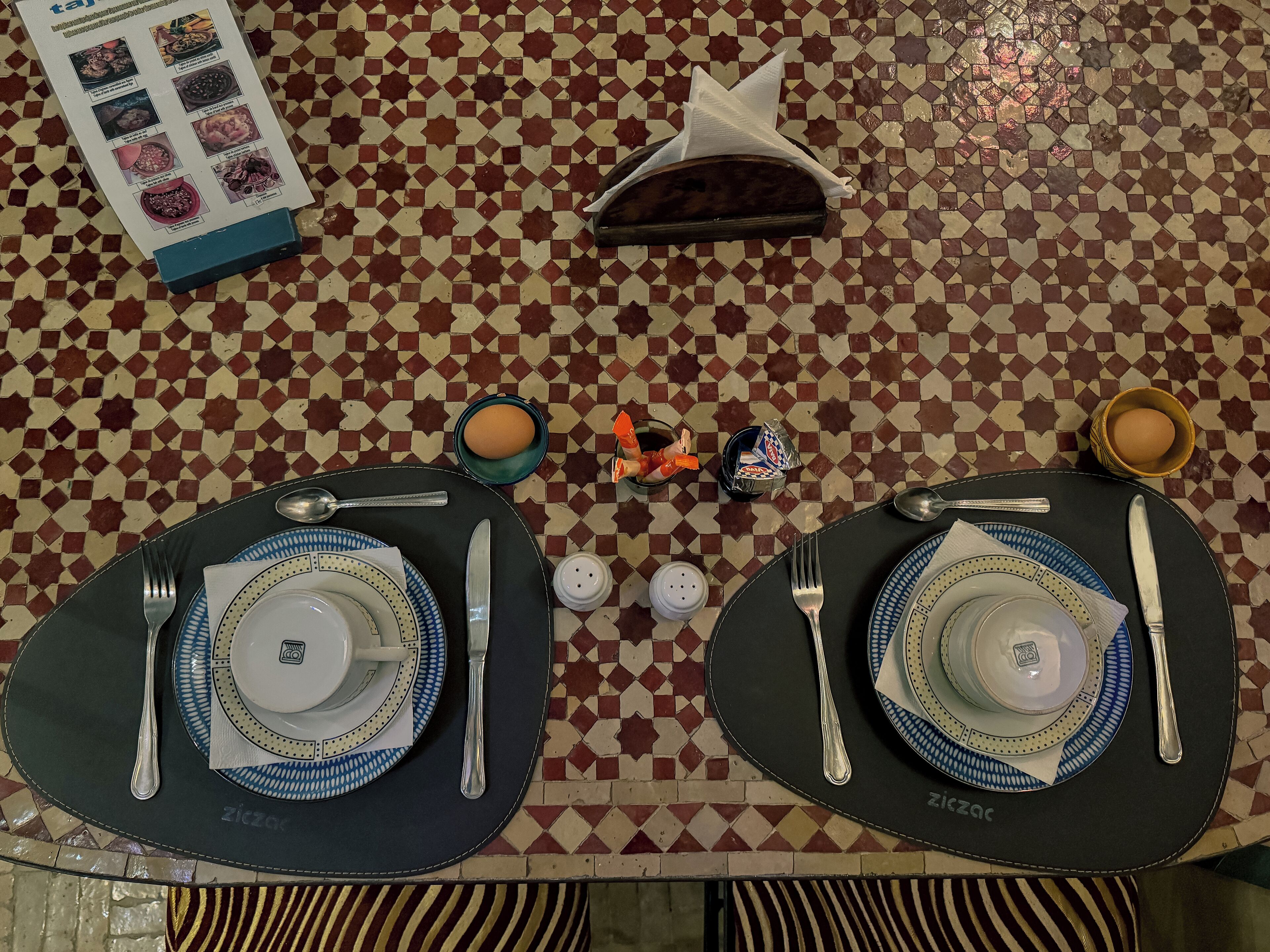 A dining table set with plates, cutlery, and condiments, with a menu and napkin holder on the table.