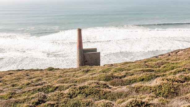 Een kustlandschap met een vuurtoren op een grasheuvel met uitzicht op de oceaan.