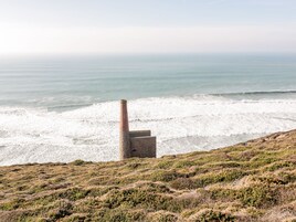 A coastal landscape with a lighthouse structure on a grassy hill overlooking the ocean.