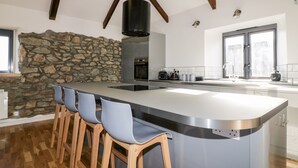 Een moderne keuken met een groot schiereiland, barstoelen, een accentmuur van steen en een hoge plafond met zichtbare balken.