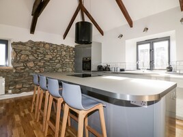 A modern kitchen with a large island, bar stools, a stone accent wall, and a high ceiling with exposed beams.