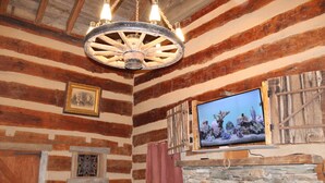 A rustic room with wooden walls, a stone fireplace, a wooden ceiling with a wheel chandelier, and a mounted television. - Step back in time a charming 1880 historic cabin (Jonesborough)