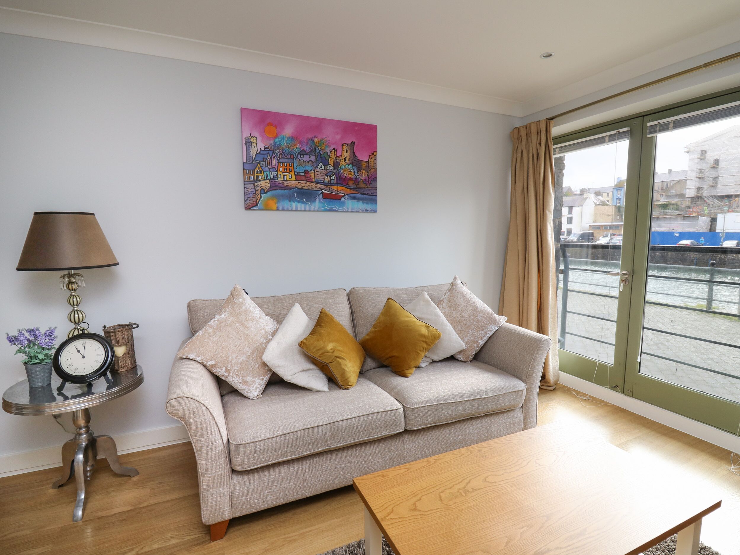 A living room with a sofa, a table, a lamp, a clock, and a painting.