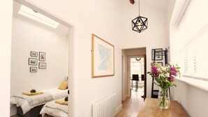Un pasillo con suelo de madera, un radiador blanco, un mapa enmarcado en la pared y una mesa de madera con un jarrón de flores.