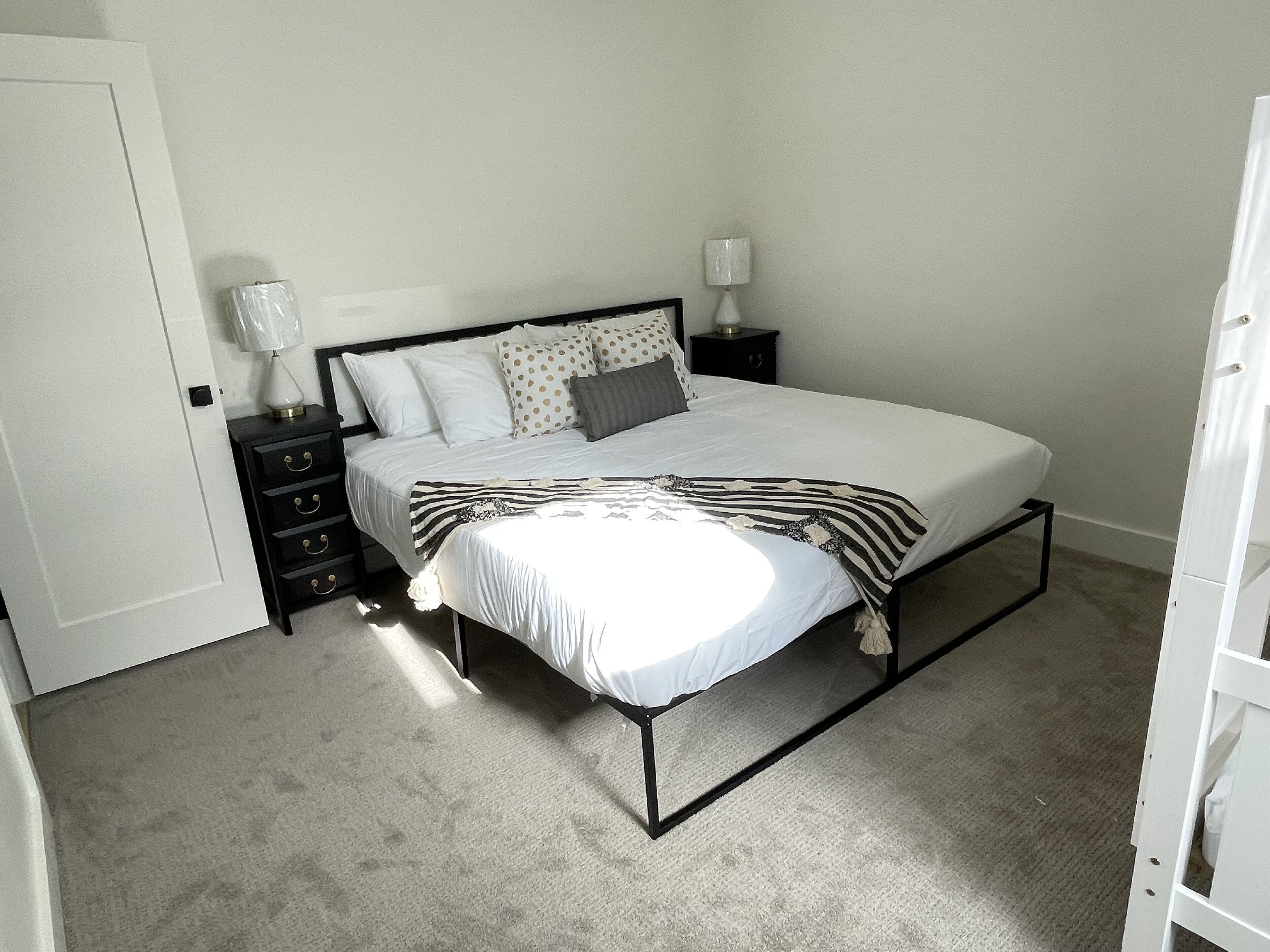 A bedroom with a bed, two bedside tables, a nightstand, and a door.