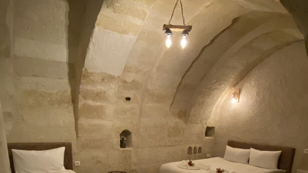Une pièce chaleureuse et faiblement éclairée, avec deux lits, une petite table et un tapis décoratif.