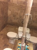 A bathroom with a shower, two toilets, and a sink.
