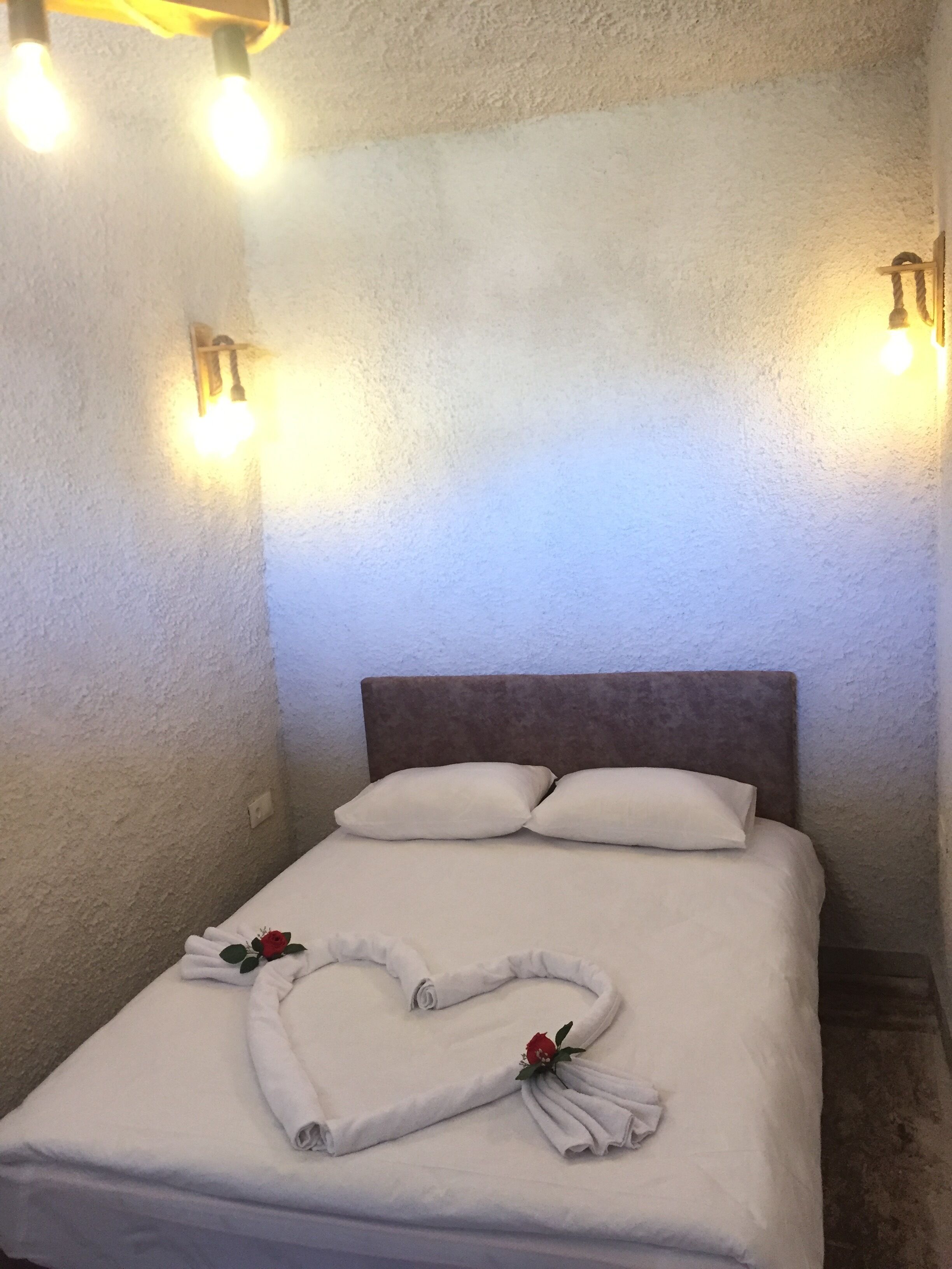 A neatly made bed with white linens and two pillows, a headboard, and two wall-mounted light fixtures.